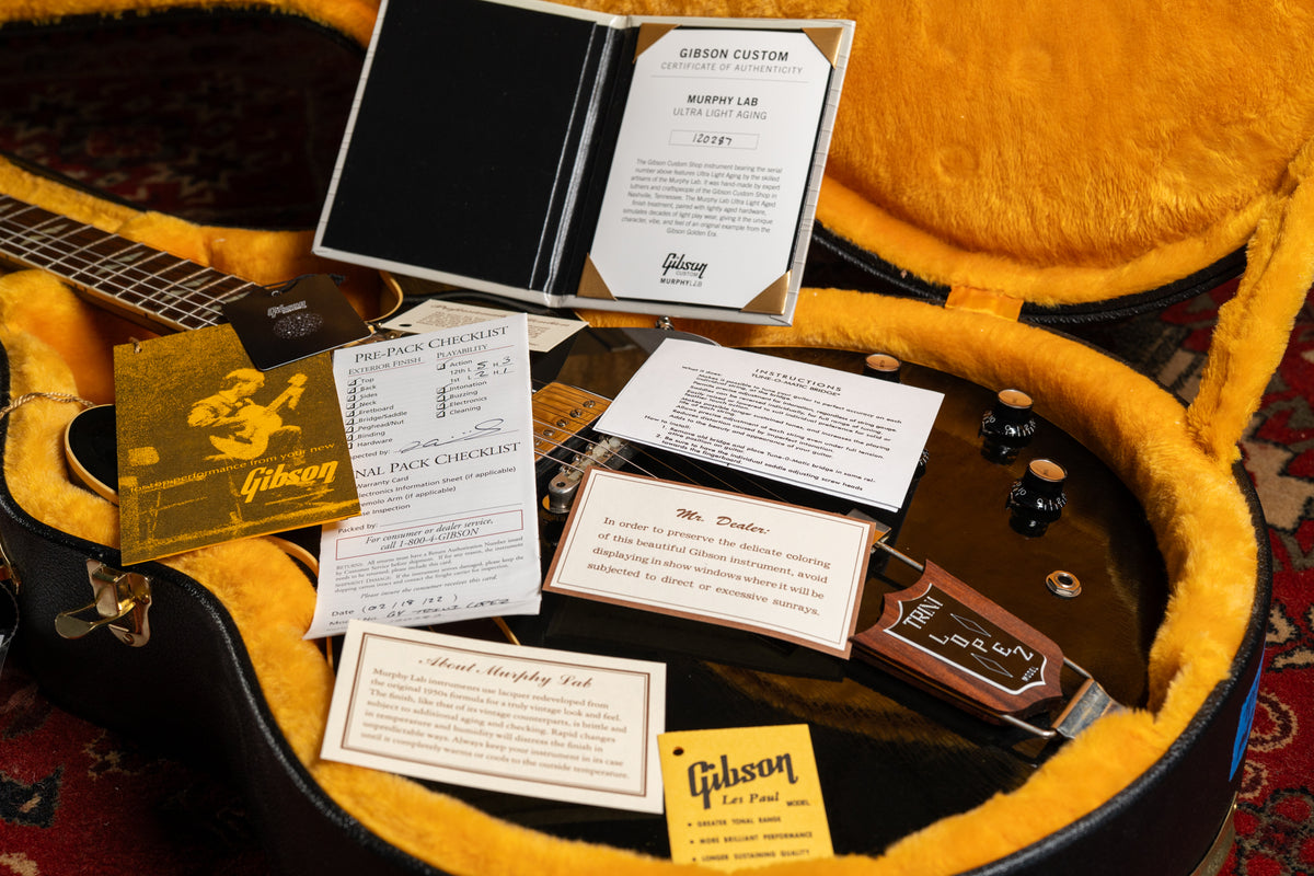 The ebony guitar body, with its Trini Lopez tailpiece and black control knobs, rests in a yellow-lined case surrounded by paperwork.