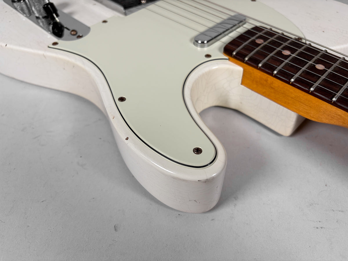 Close-up of the Olympic White Telecaster's lower bout, showing finish checking, dings, and the light green pickguard with a black border.