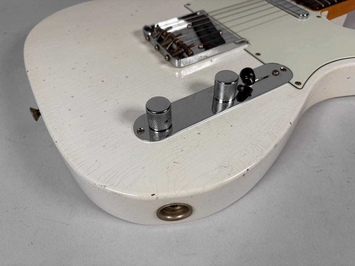Close-up of the lower body of a white Telecaster, showing heavy finish checking, two chrome knurled knobs, and a black switch tip.