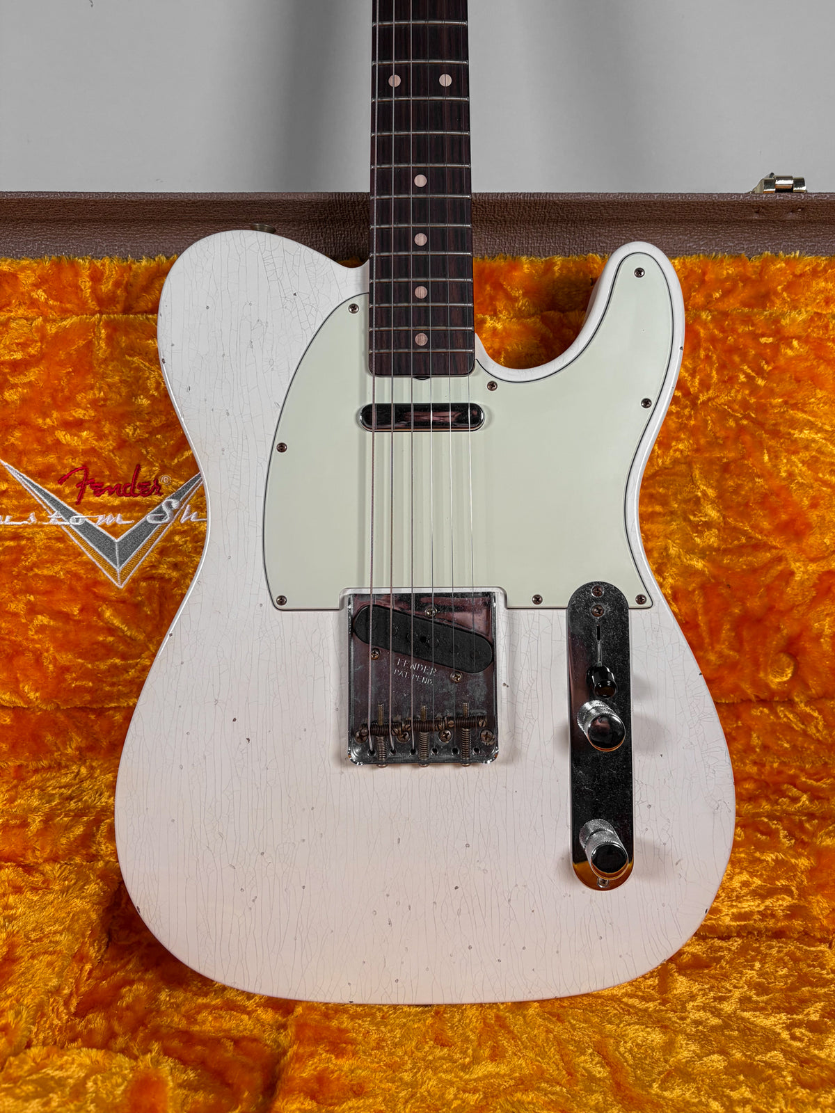 Full-frame view of an Olympic White Telecaster with heavy finish checking, a mint green pickguard, and aged chrome hardware.