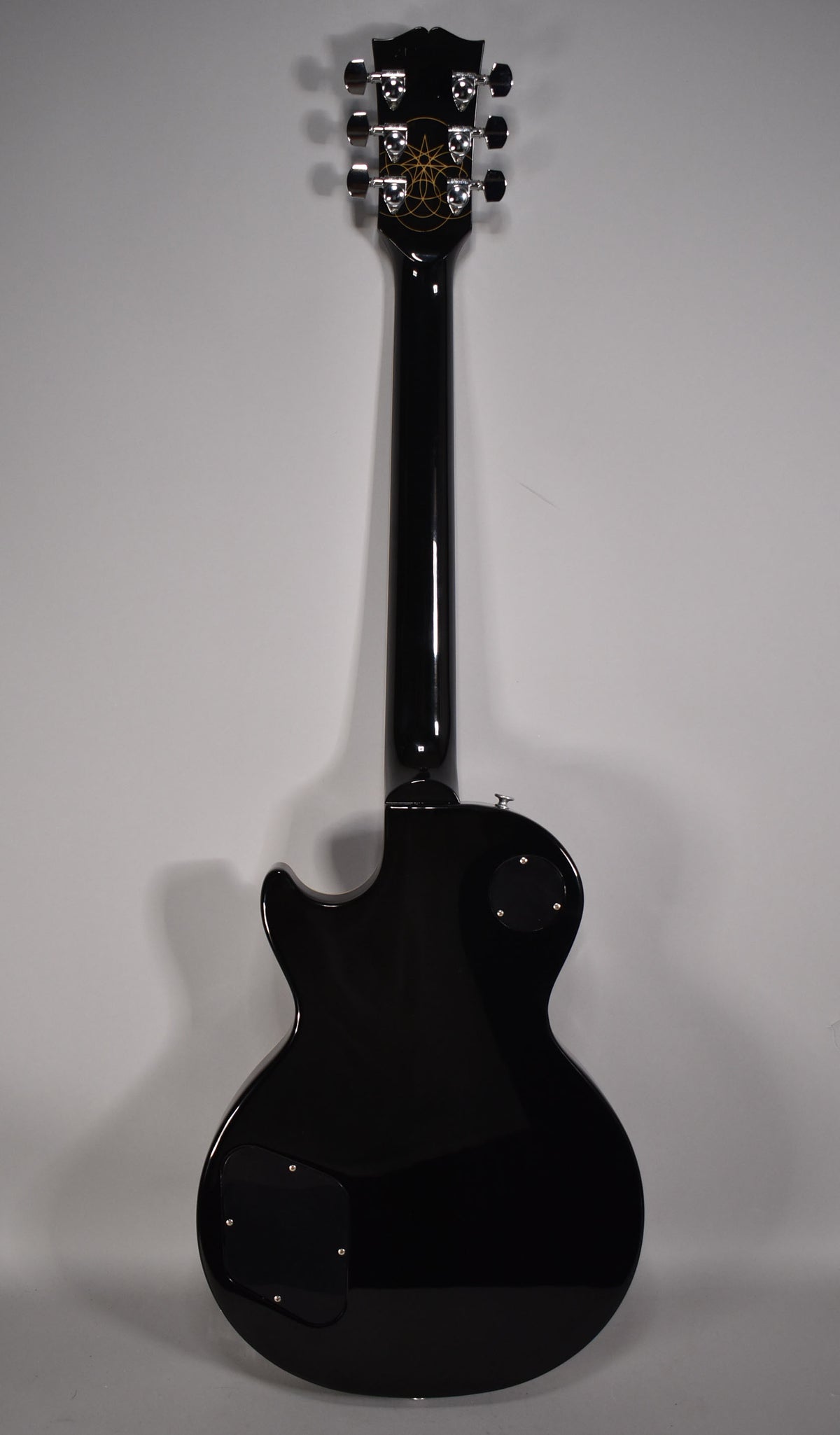 The guitar's back is glossy black, with a gold geometric pattern on the headstock and chrome tuners.