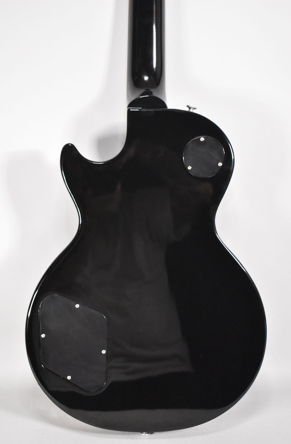 The guitar's glossy black back is shown, with two black control cavity covers and a strap button at the bottom.