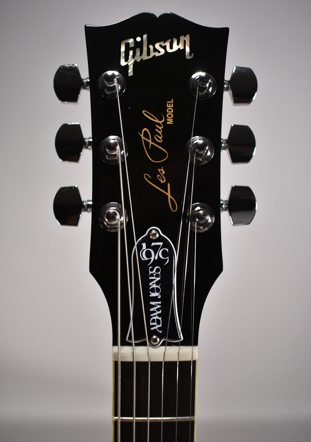 The guitar's black headstock, with chrome tuners and a white truss rod cover, is centered, showing the top of the fretboard.
