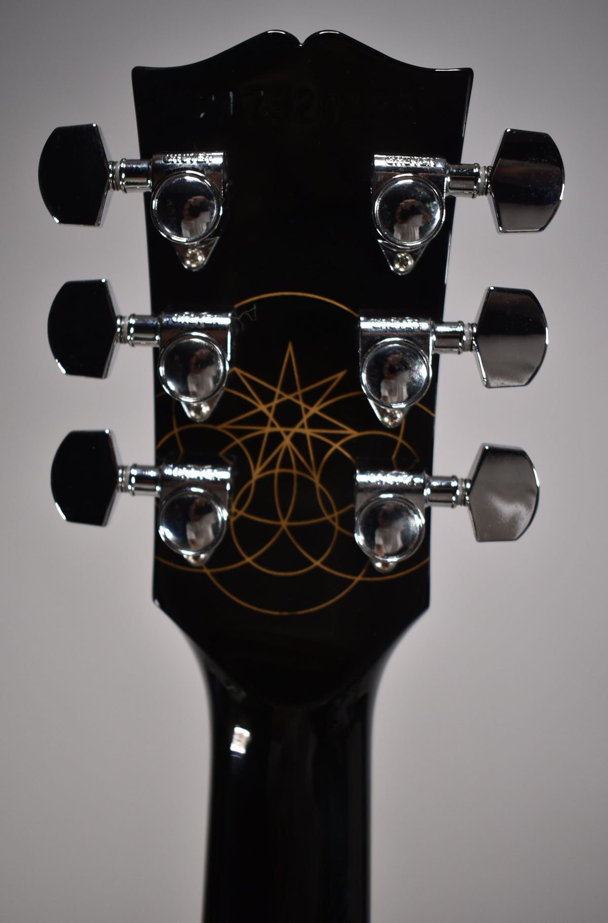 Rear view of the black headstock and neck, showing six chrome tuners and a gold geometric design on the headstock.