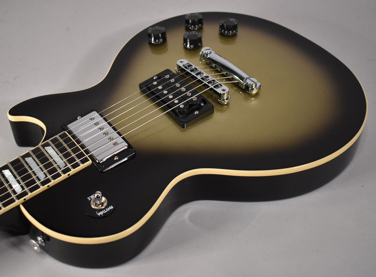 The guitar's body, angled from the lower bout, shows a matte silverburst finish, chrome hardware, and cream binding.