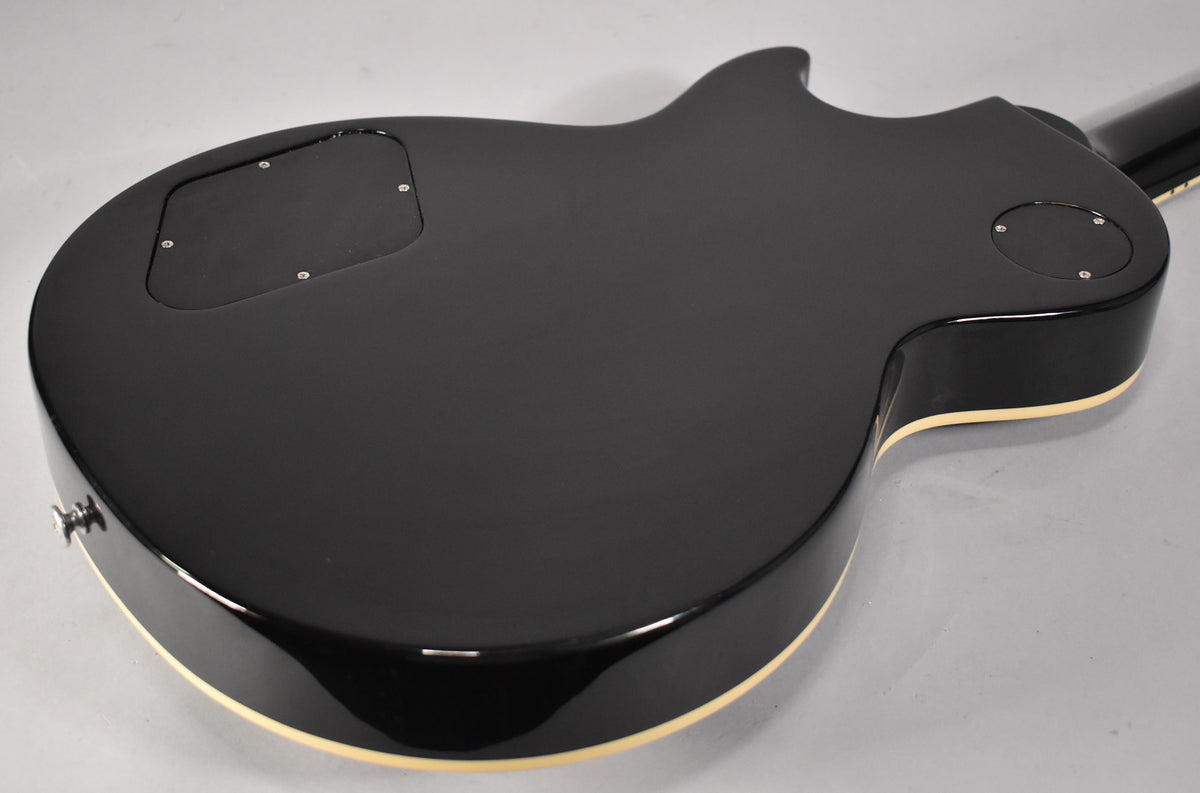 The back of a black guitar with cream binding, showing the control cavity and output jack.