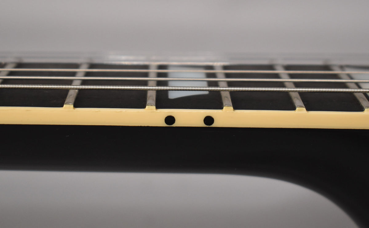 Close-up of the guitar's fretboard from the side, showing frets, strings, cream binding, and two black side dot markers.