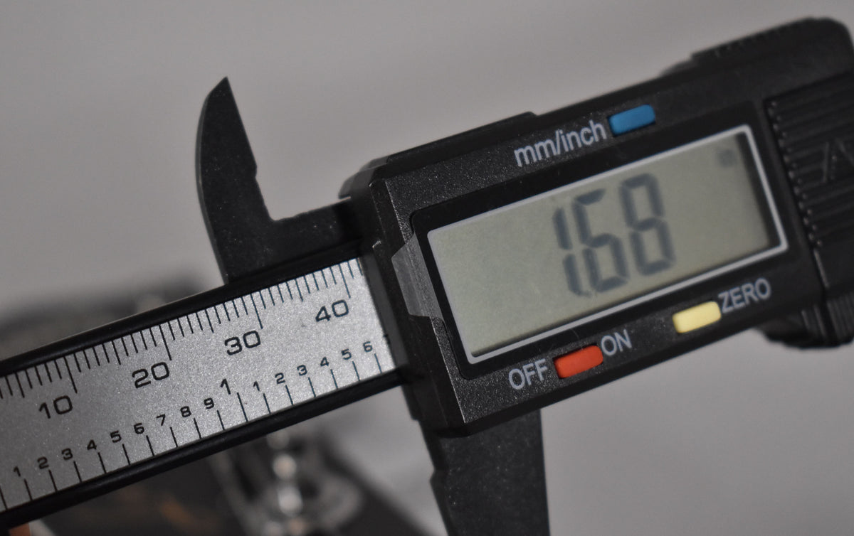 Close-up of the guitar's nut width being measured by a digital caliper, displaying "1.68" inches on its screen.