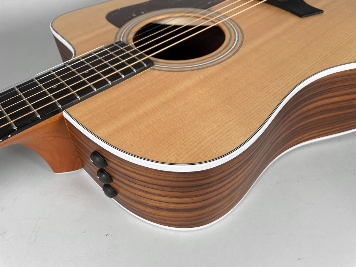 Close-up of the guitar's natural finish body and dark wood sides with white binding, showing three black control knobs and the cutaway.