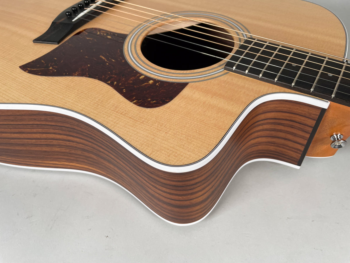 Close-up of the natural finish acoustic guitar's lower bout and cutaway, showing the dark wood grain and white binding.