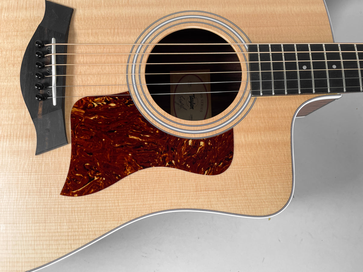 Close-up of the natural finish acoustic guitar's body, showing the soundhole, tortoise pickguard, black bridge, and lower fretboard.