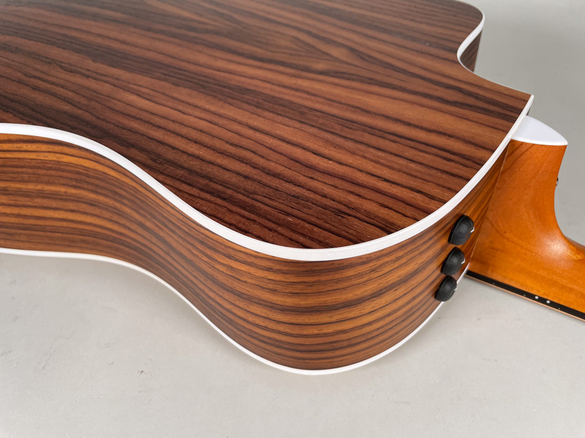 Close-up of the guitar's lower bout and cutaway, showing the dark wood grain, white binding, and three black control knobs.