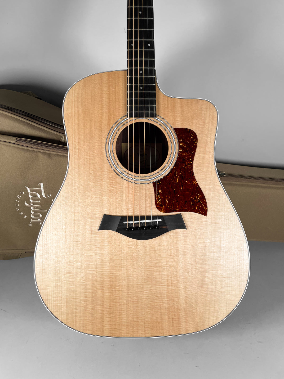 Full-front view of a natural finish acoustic guitar with a cutaway, dark tortoiseshell pickguard, and black bridge.
