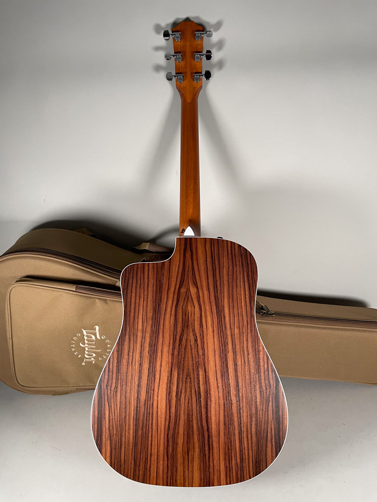 The acoustic guitar's back and neck are visible, showing a dark brown striped wood grain and six chrome tuners.