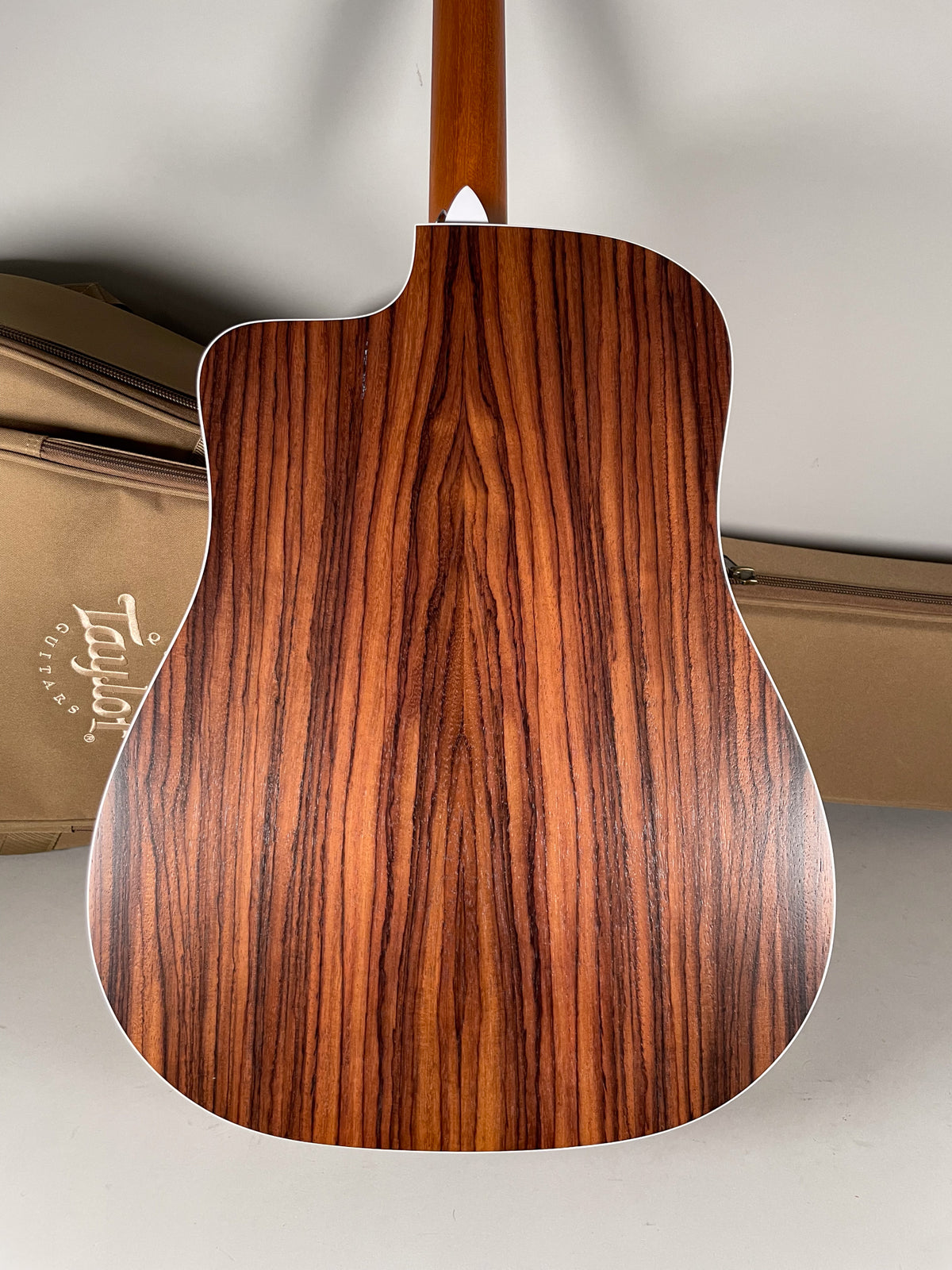 The guitar's back shows a natural wood grain with dark brown stripes, a cutaway, and a light-colored binding.