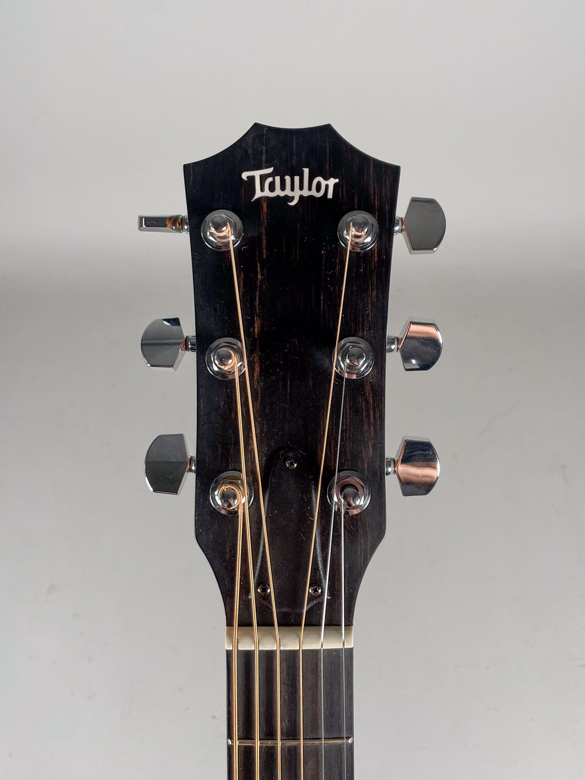 Close-up of the dark wood headstock with a white logo, six chrome tuners, and strings, showing some light wear.