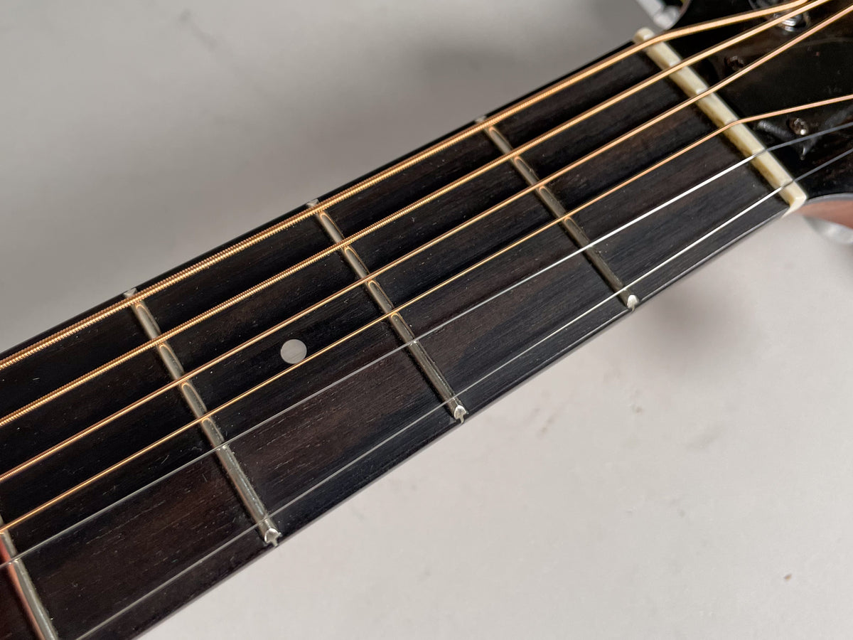 Close-up of the dark fretboard with light strings, showing a single white dot inlay at the 7th fret and a cream-colored nut.