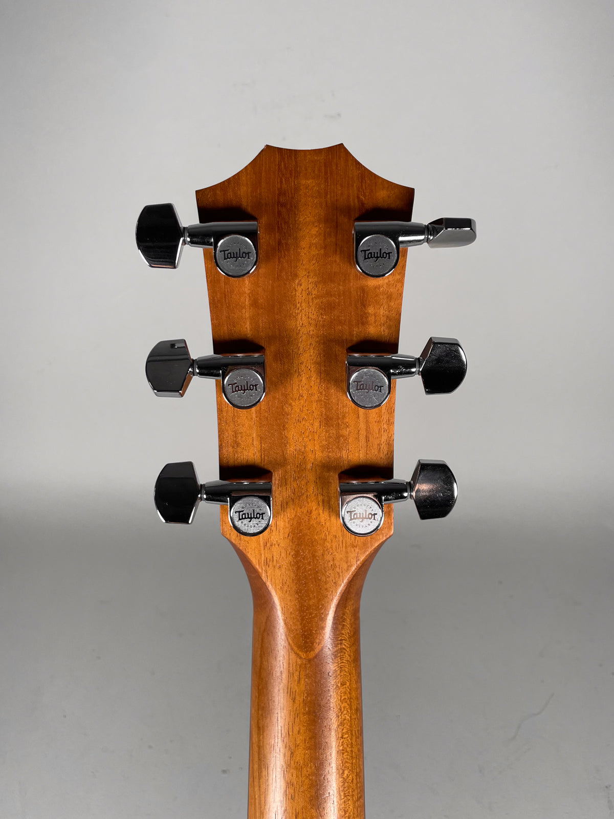 Rear view of the guitar's headstock and upper neck, showing six chrome tuners with black buttons on a natural wood finish.