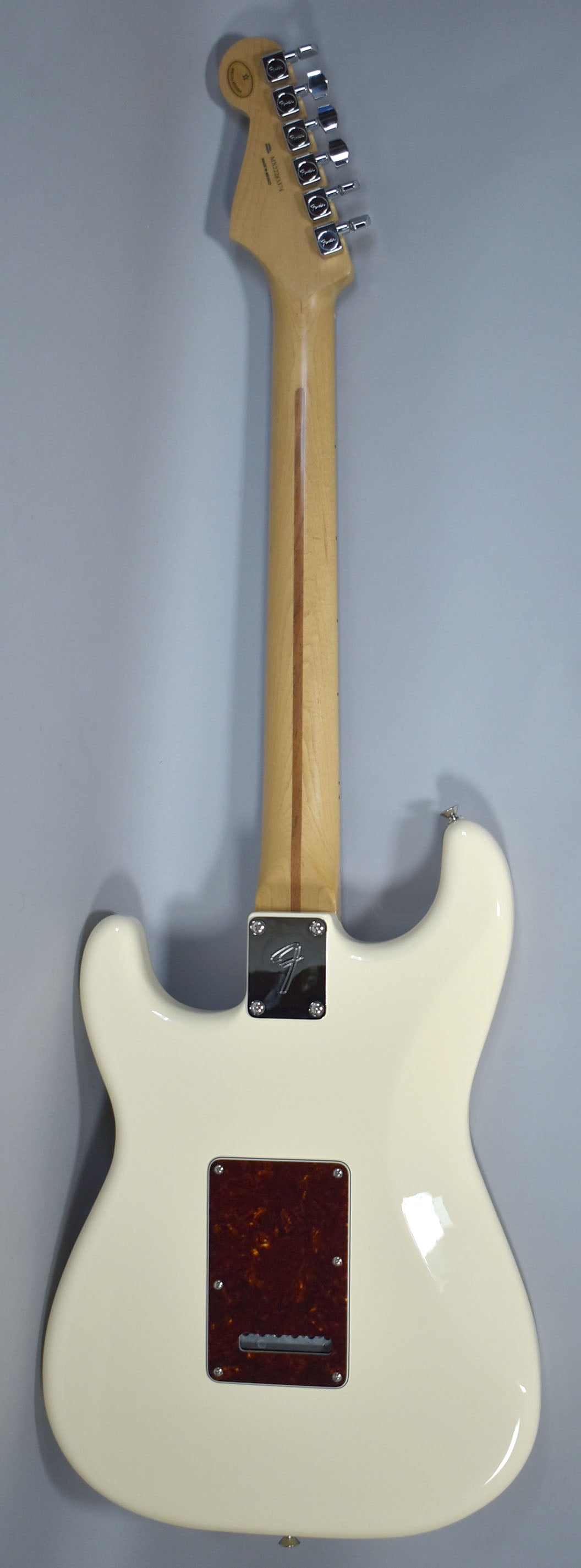Full rear view of an Olympic White Stratocaster with a maple neck, chrome tuners, a chrome neck plate, and a tortoiseshell tremolo cover.