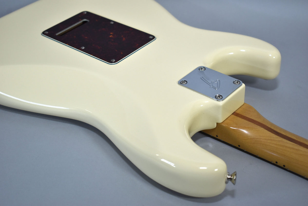 The back of an Olympic White Stratocaster body, showing the tortoiseshell tremolo cover, chrome neck plate, and maple neck.