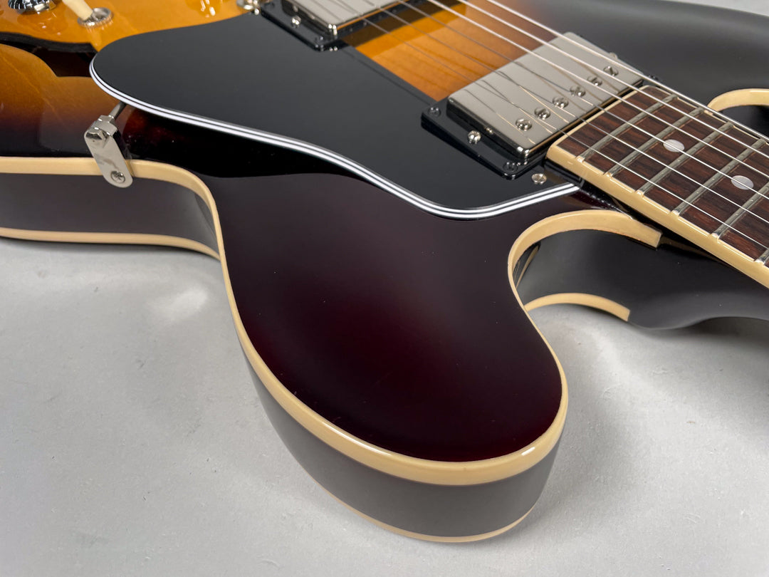 Close-up of the guitar's lower bout, showing the dark sunburst finish, cream binding, black pickguard, and chrome humbucker.