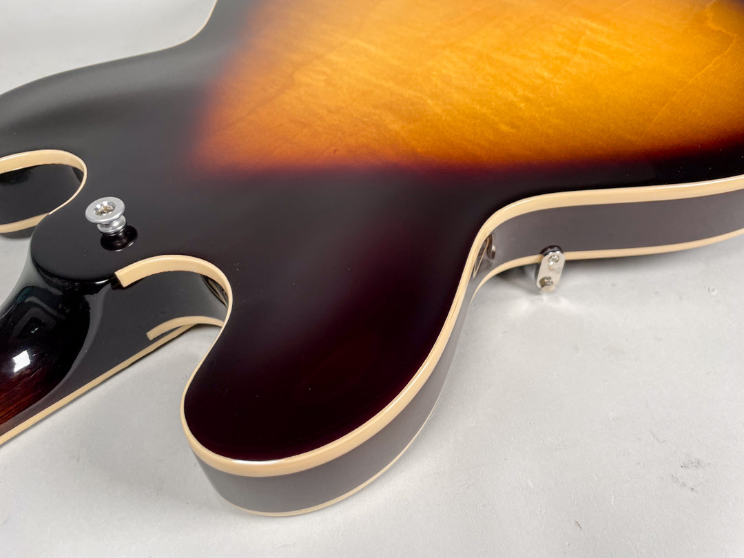 The guitar's sunburst body, with cream binding, is angled to show the lower bout, neck heel, and strap buttons.