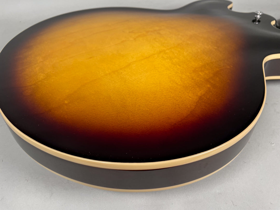 The guitar's sunburst back, with a glossy finish and cream binding, shows a few minor surface scuffs and dust.