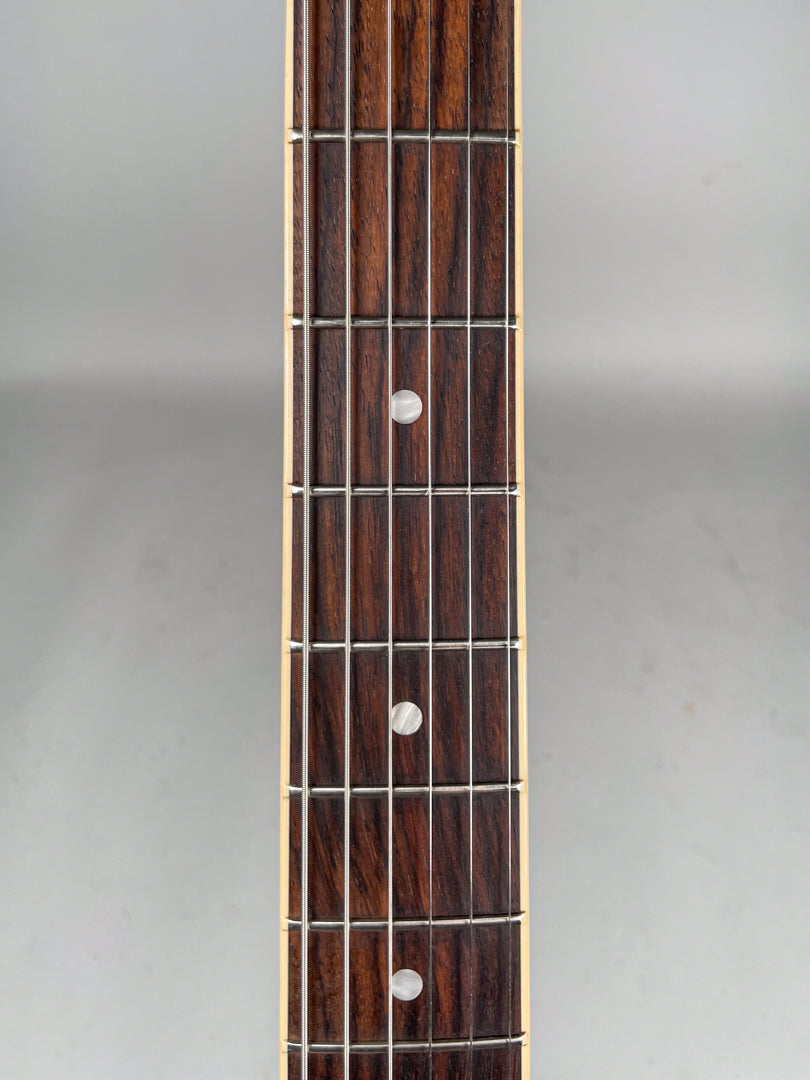 Close-up of the dark rosewood fretboard with three pearloid dot inlays and shiny frets, framed vertically.