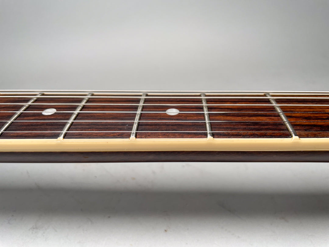 Close-up of the guitar's dark rosewood fretboard with white dot inlays and cream binding, viewed from the bass side.