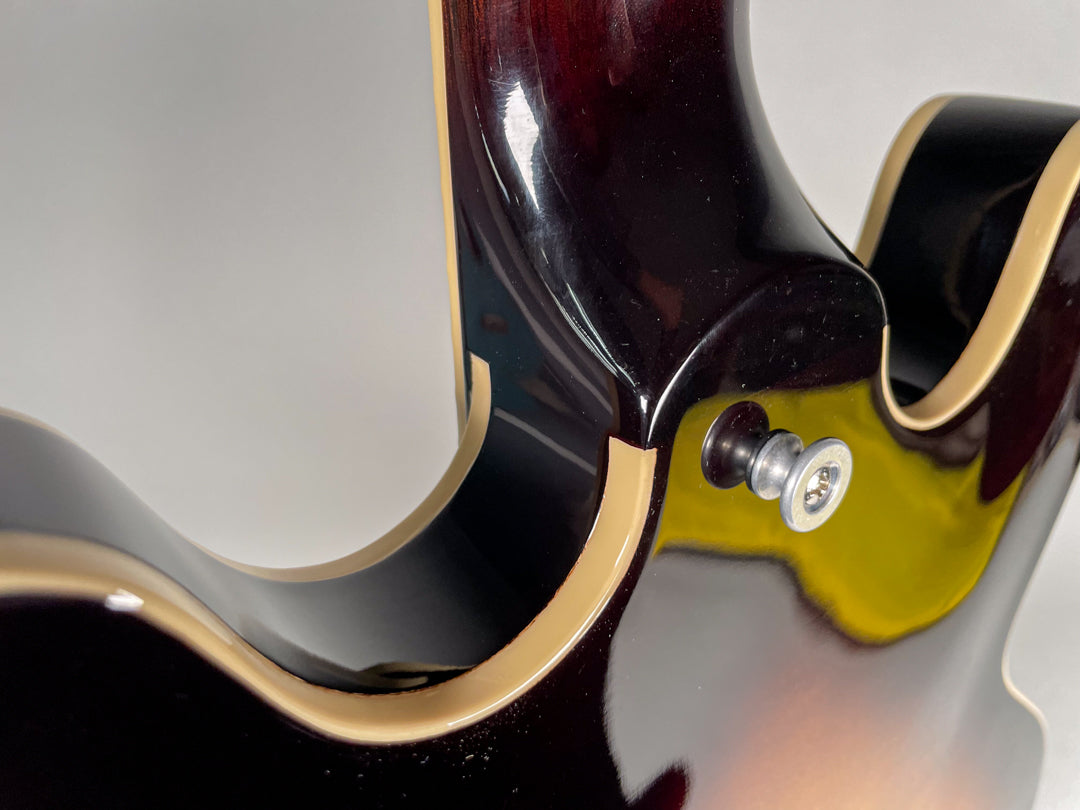 Close-up of the guitar's sunburst body and neck joint, showing the lower strap button and cream binding.