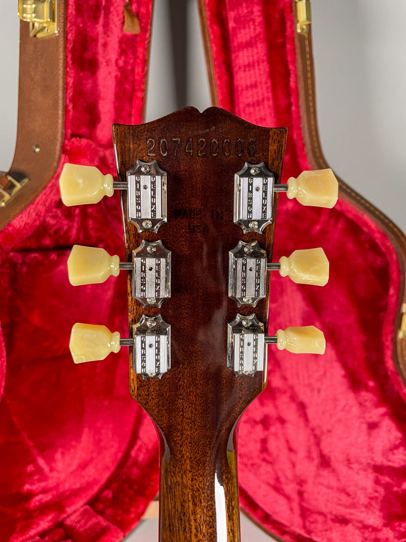 The back of the guitar's headstock and upper neck, showing six cream-colored tuning pegs and chrome tuners, against a red velvet case lining.