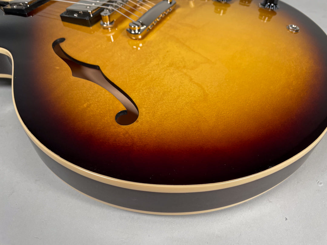 Close-up of the lower bout of a glossy sunburst semi-hollow electric guitar, showing an f-hole and cream binding.