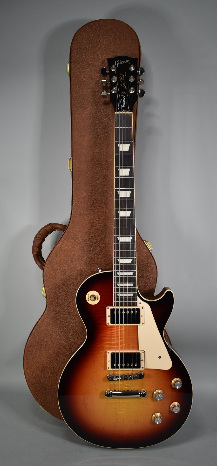 Full-length view of a sunburst electric guitar with cream binding, trapezoid inlays, and a brown hard case behind it.