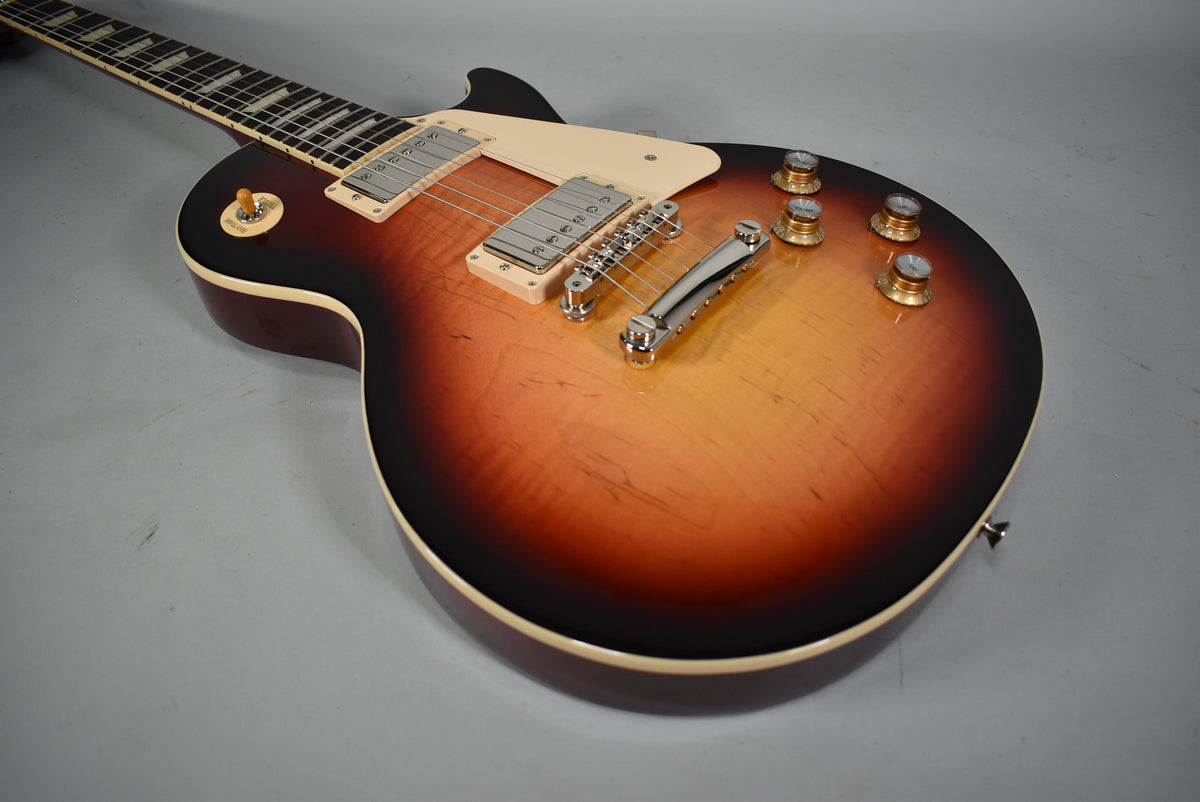 The guitar's sunburst body, with cream binding, is angled from the upper left, showing chrome hardware, cream pickup rings, and gold top hat knobs.
