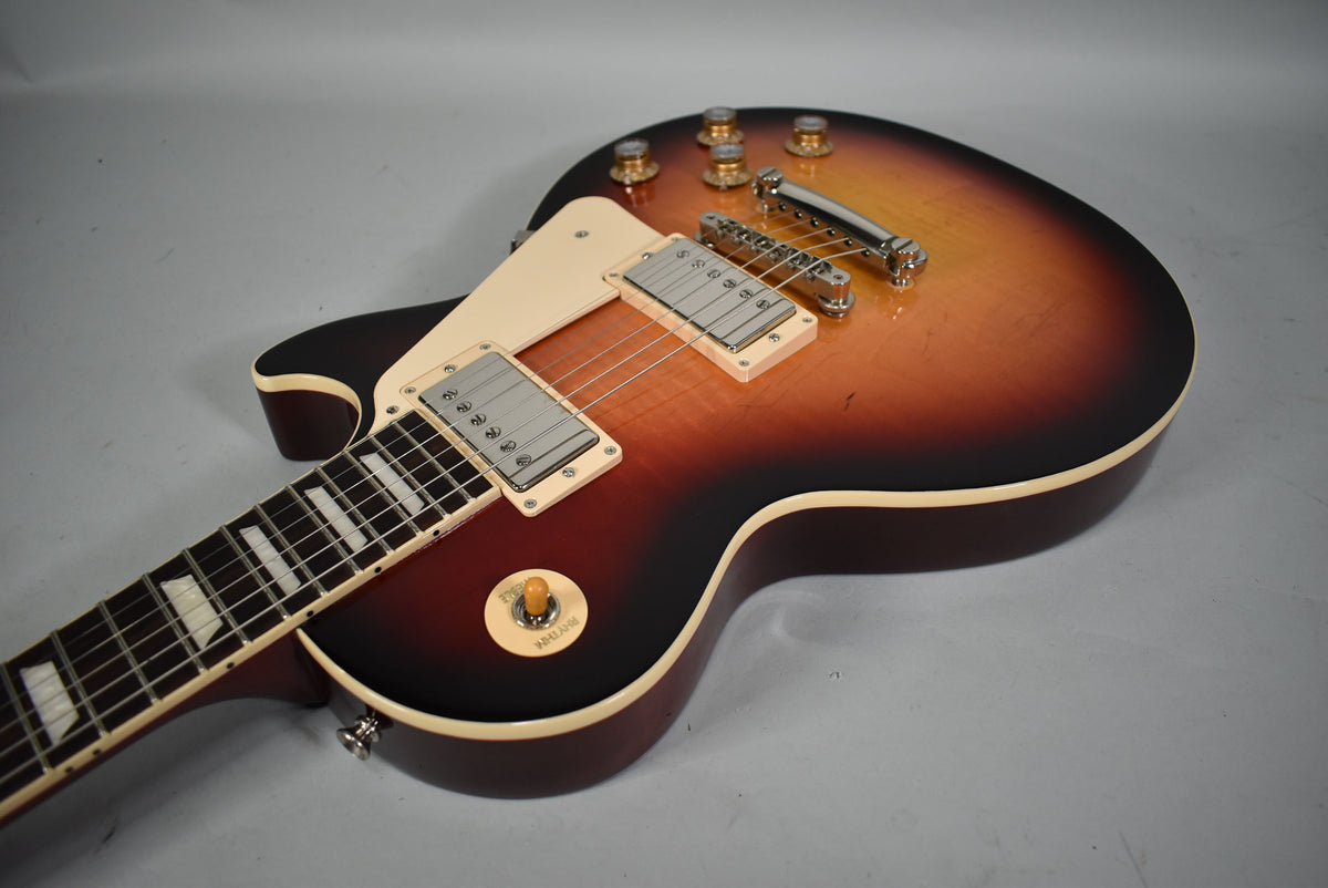 This Les Paul Standard in Sunburst has a cream pickguard, two humbuckers, a tune-o-matic bridge, and gold top hat knobs.