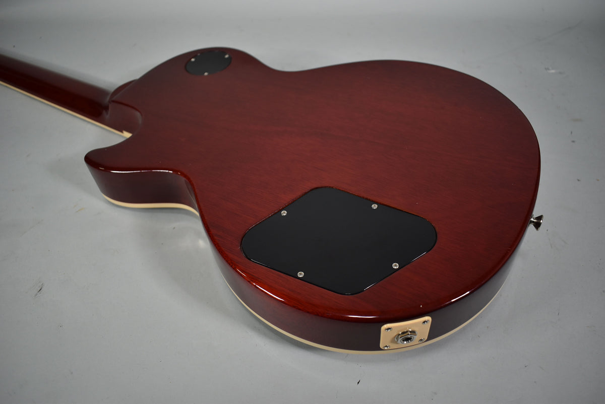 The back of a cherry sunburst guitar body, showing the control cavity cover, output jack, and a strap button.
