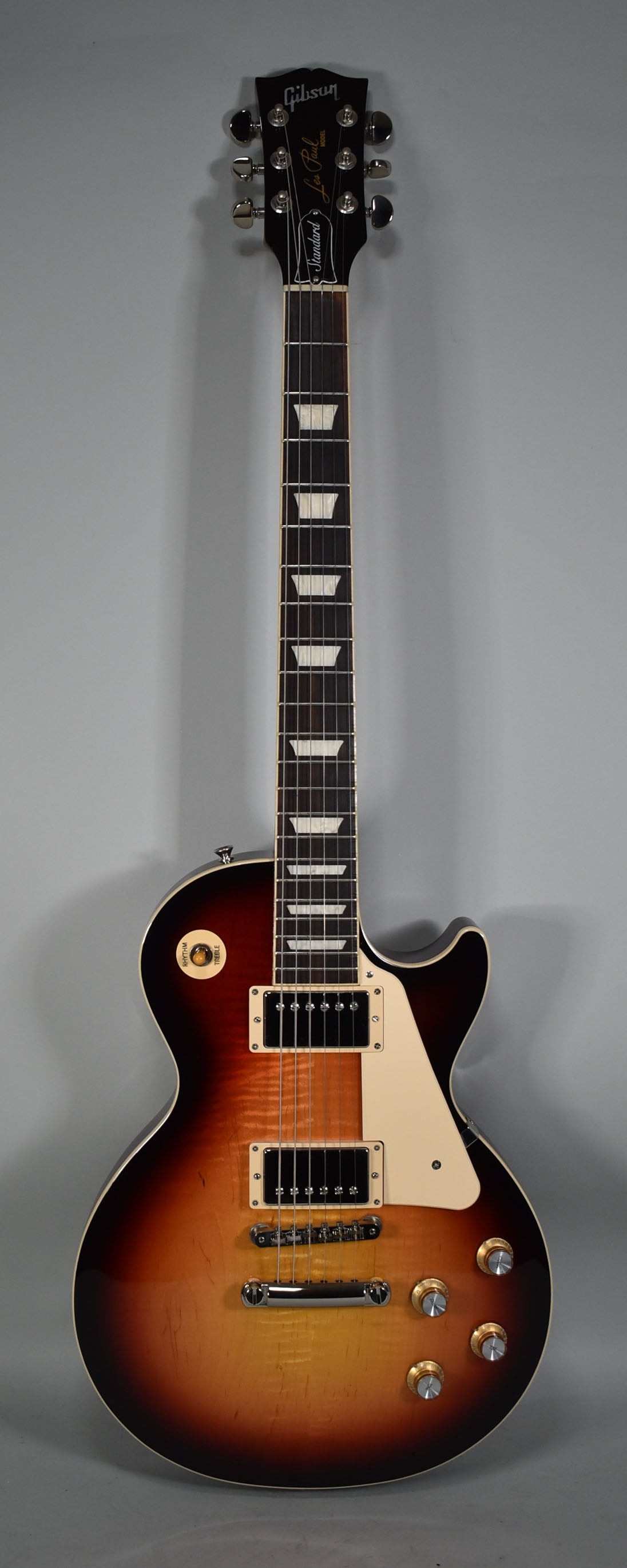 Full front view of a sunburst electric guitar with a dark headstock, trapezoid fretboard inlays, and four gold control knobs.