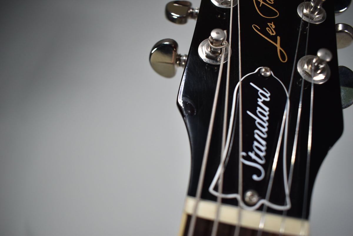 Close-up of the glossy black headstock, angled to show the top three tuners and a small ding near the low E string post.