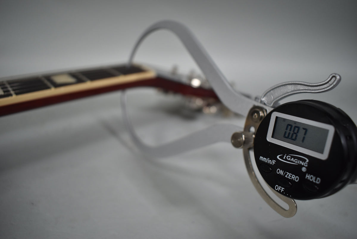 Close-up of the guitar's dark red neck and fretboard with trapezoid inlays, measured by a digital caliper showing "0.87".