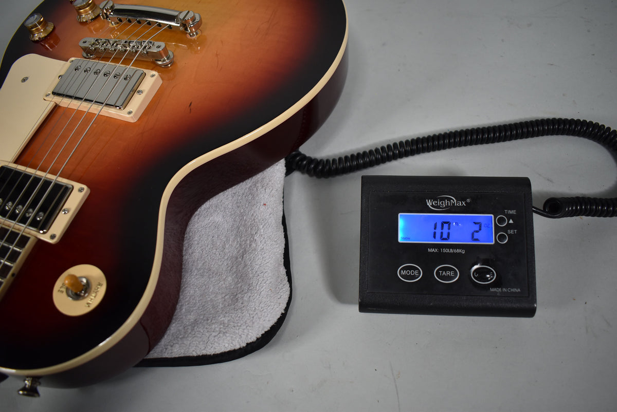 The Les Paul's sunburst body, with cream binding and pickup rings, rests on a towel next to a scale displaying "10" 2".