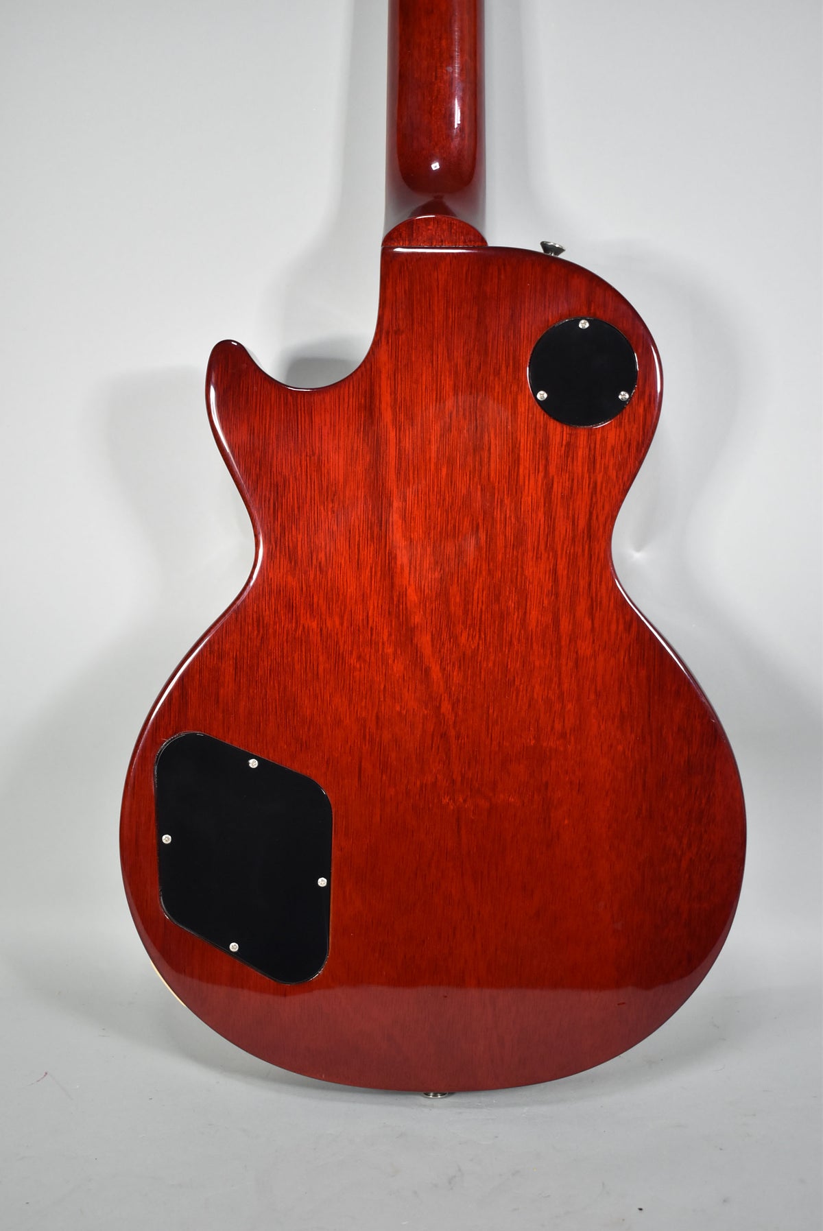 The back of a cherry red electric guitar, showing the neck joint, two black control cavity covers, and a strap button.