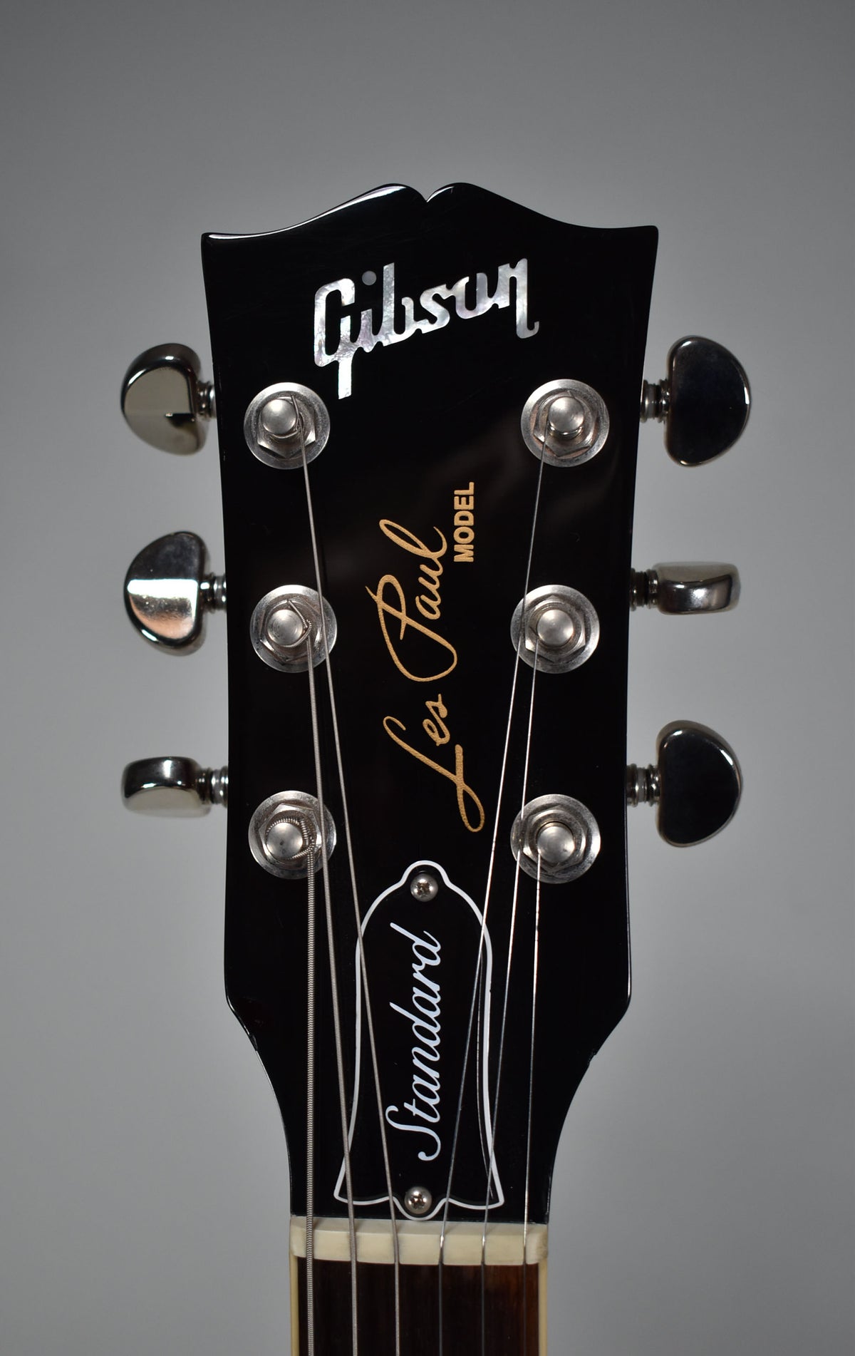 Close-up of the glossy black headstock, showing six chrome tuners, the top of the nut, and the first fret of the dark fretboard.