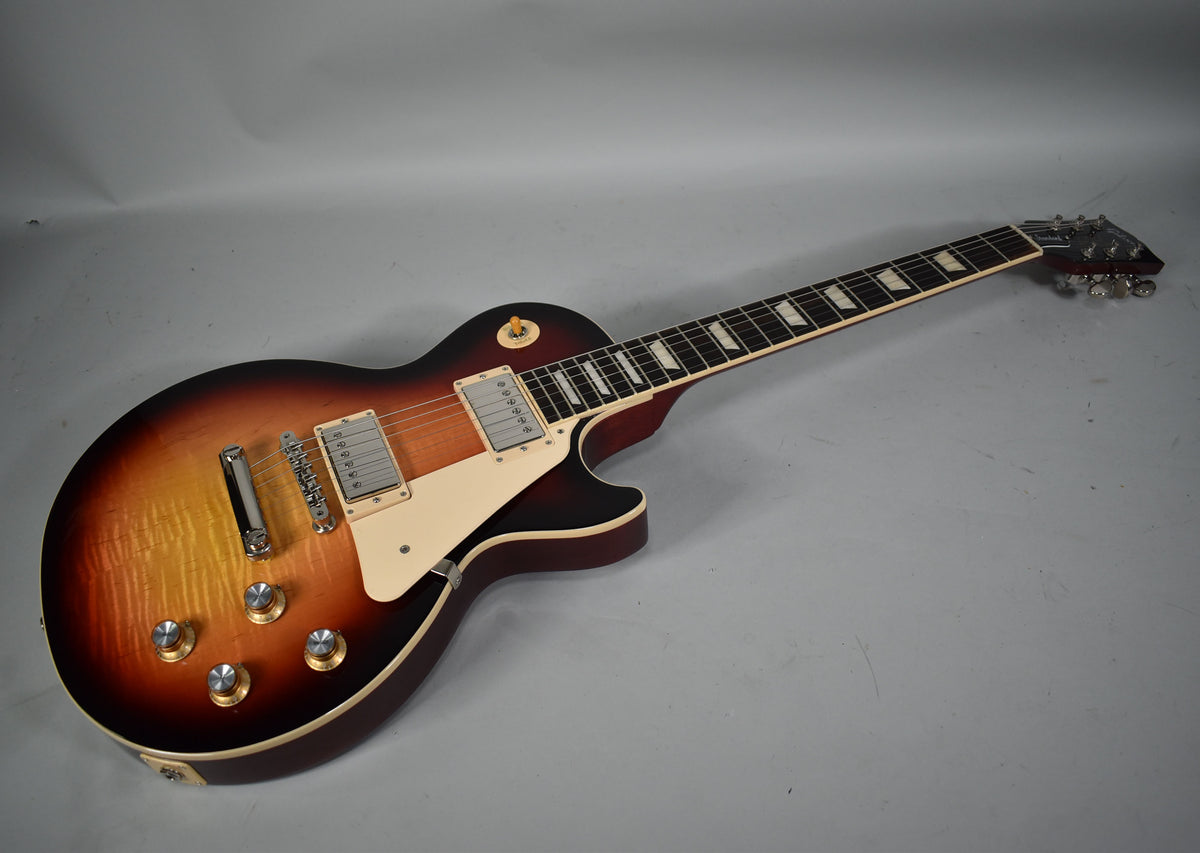Full view of a Les Paul in sunburst, angled left, showing the flame maple top, cream binding, and nickel hardware.