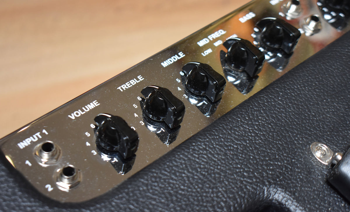 Close-up of the amp's shiny chrome control panel, showing black numbered knobs for Volume, Treble, Middle, and Mid Freq.