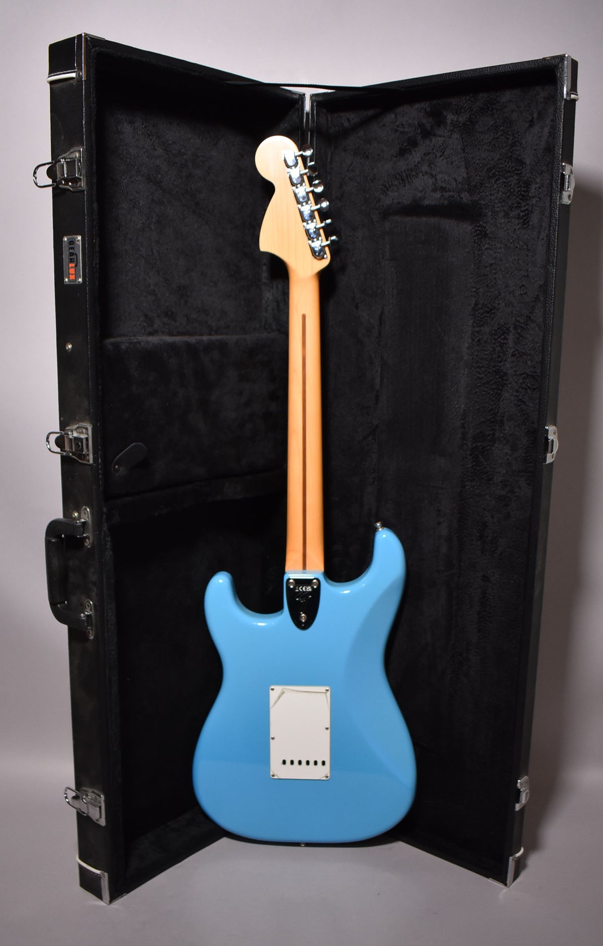 The Maui Blue Stratocaster is shown from the back, standing upright in its open, black plush-lined hard case.
