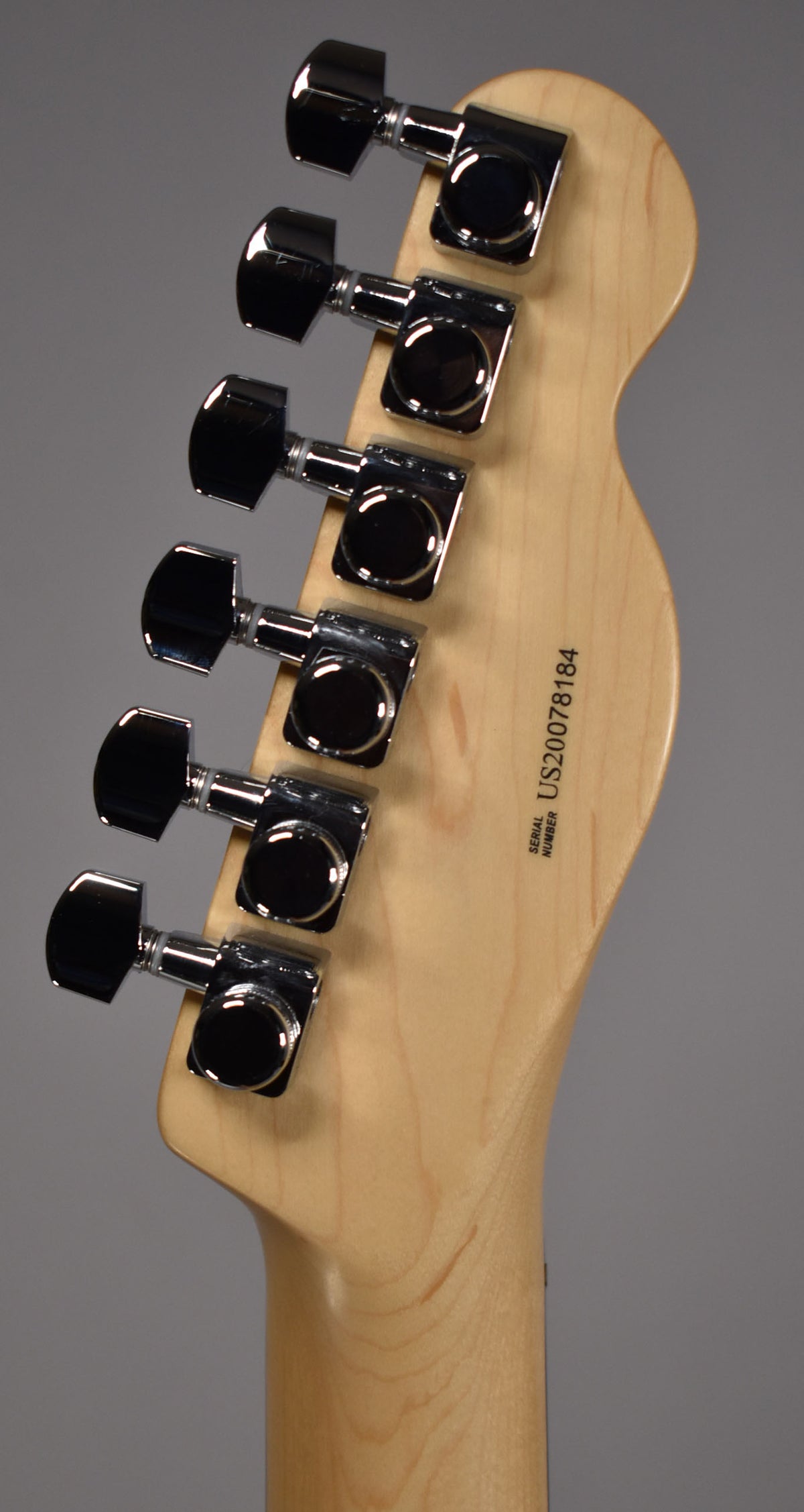 The back of a light wood headstock with six chrome tuning machines, angled to show the left-handed orientation.