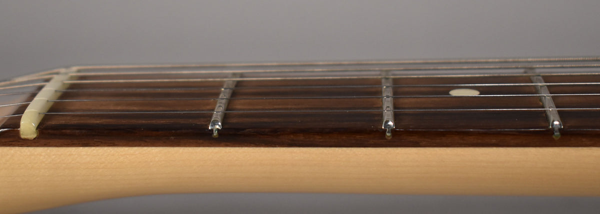 Close-up of the guitar's dark fretboard and light maple neck, showing the nut, frets, and strings from a side angle.