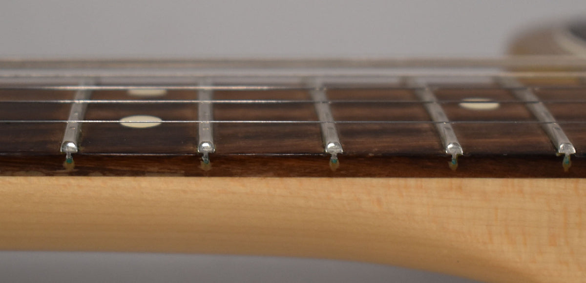 Close-up of the guitar neck and fretboard, showing five frets with round pearloid inlays and a light maple neck.
