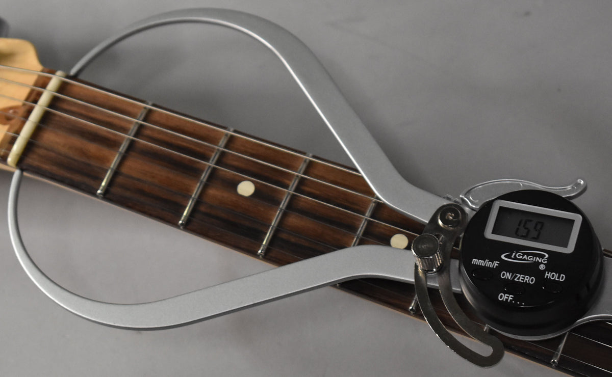 A digital gauge measures the dark rosewood fretboard with light fret markers and frets, showing "1.59" on its screen.