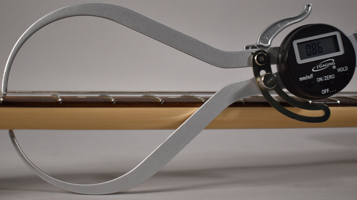A digital caliper measures the neck relief of the guitar's light-colored maple neck and dark fretboard, displaying "0.86".